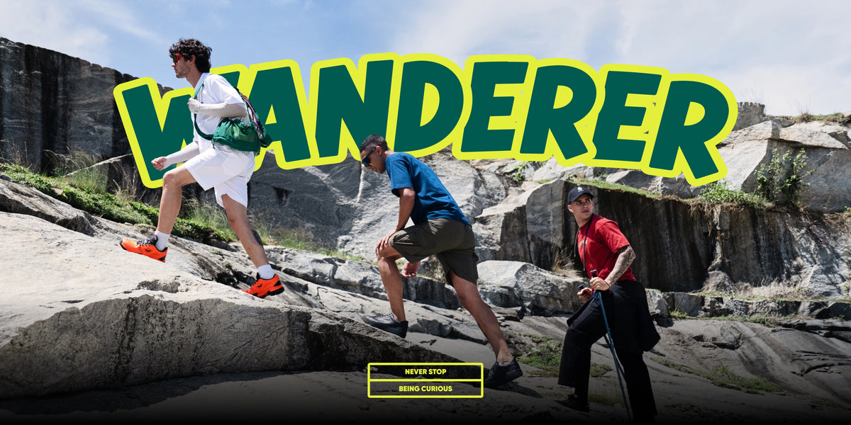 Three people climbing rocky cliffs outdoors under a large yellow outlined 'WANDERER' text overlay. The scene includes a man in white and orange running shoes, a man in a blue shirt and shorts, and a man in a red shirt and black pants.